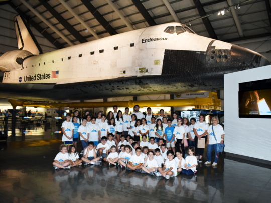 A group of campers sit below the US Endeavor space shuttle.