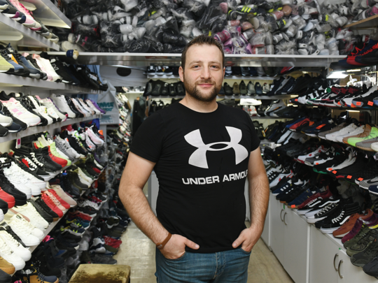 A man standing with his hands in his pockets in between rows of sneakers from floor to ceiling. 