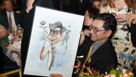 Dr. Patapoutian admires his Vrej Kassouny caricature portrait, gifted by the Gala Committee 2023
